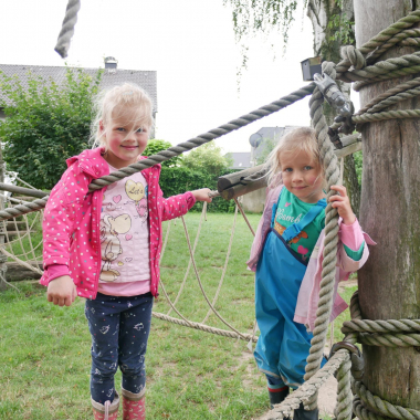 Zwei Kinder aus unserer Kindertagesstätte klettern draußen im Garten und lachen in die Kamera. Unsere pädagogischen Fachkräfte fördern spielerisch motorische, soziale und emotionale Kompetenzen. ...
