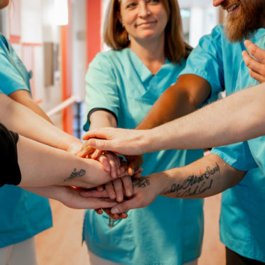 Starkes Team in der Pflege: Mehrere Pflegefachkräfte legen ihre Hände zusammen und zeigen Zusammengehörigkeit. Wir stehen für professionelle Pflege, respektvolle Zusammenarbeit und ein unterstü...
